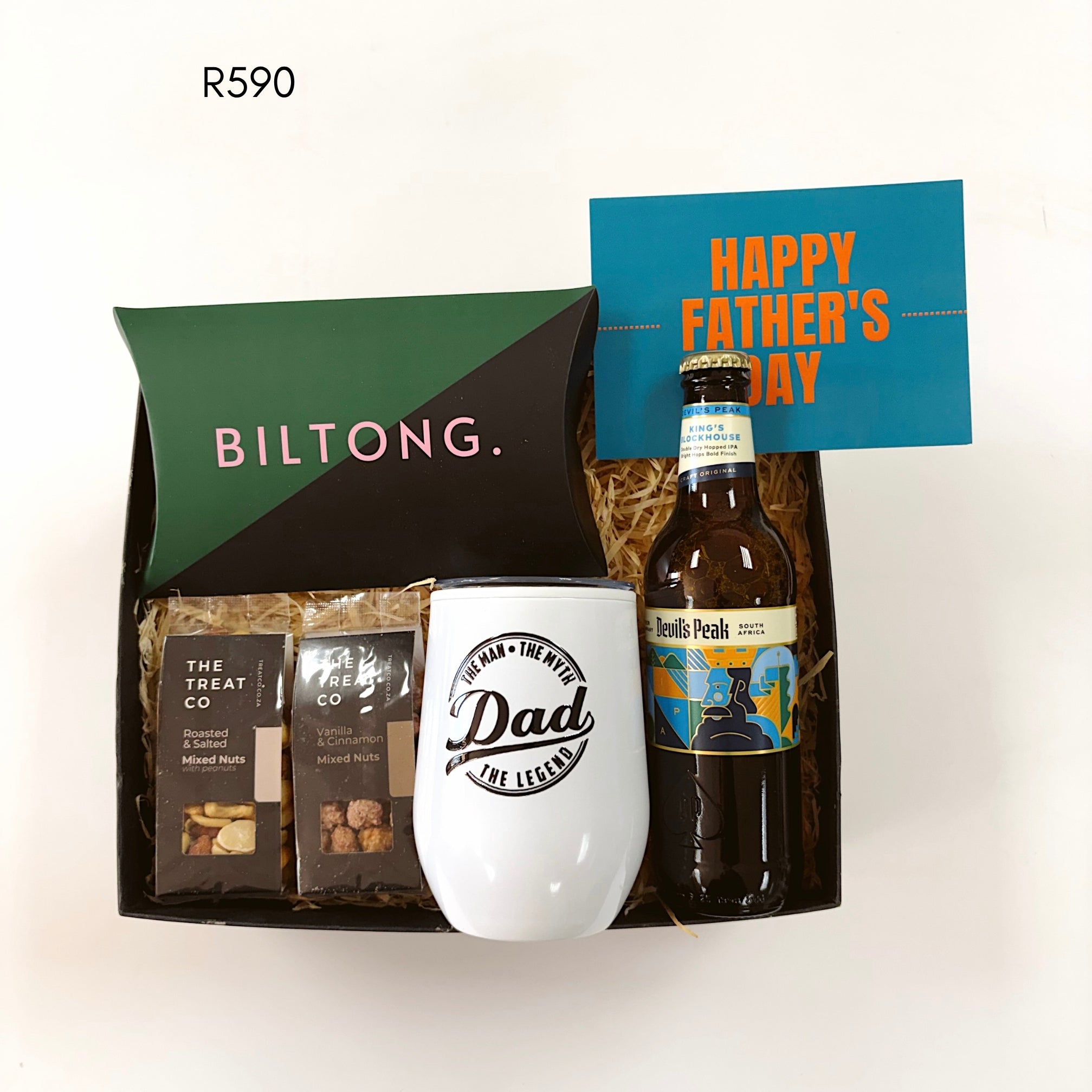 A Father's Day gift set in a black tray with shredded paper filler, featuring a green and black Biltong package, two bags of The Treat Co. mixed nut snacks, a white tumbler printed with 'Dad' in black script, a bottle of Devil's Peak beer, and a blue card that says 'HAPPY FATHER'S DAY'.