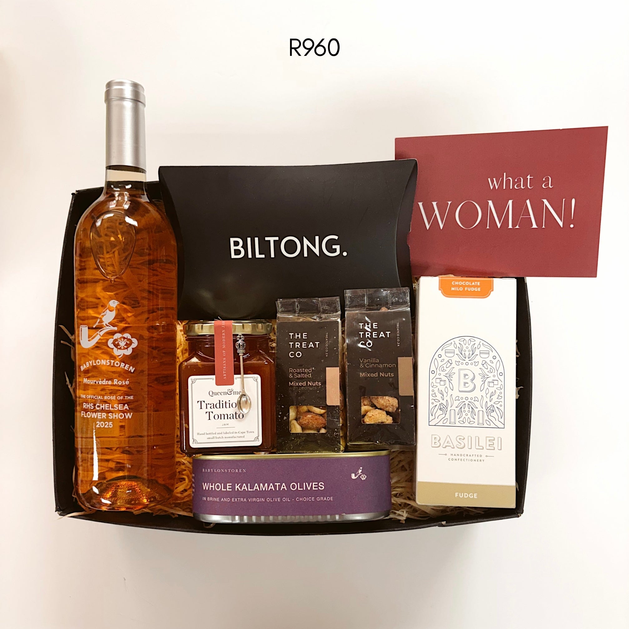 A curated gift box set from Biltong. featuring a bottle of Rosé, a jar of Traditional tomato jam, two bags of mixed nuts treats, and Basilei chocolate milo fudge on a plain white background.