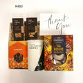 A curated gift basket set featuring a can of Plato Caribbean Mocha, a box of Vla Koekies, a box of Darling Sweet Butterscotch soft caramels, and two bags of The Treat Co mixed nuts, arranged with a white 'thank you' card on a white background.