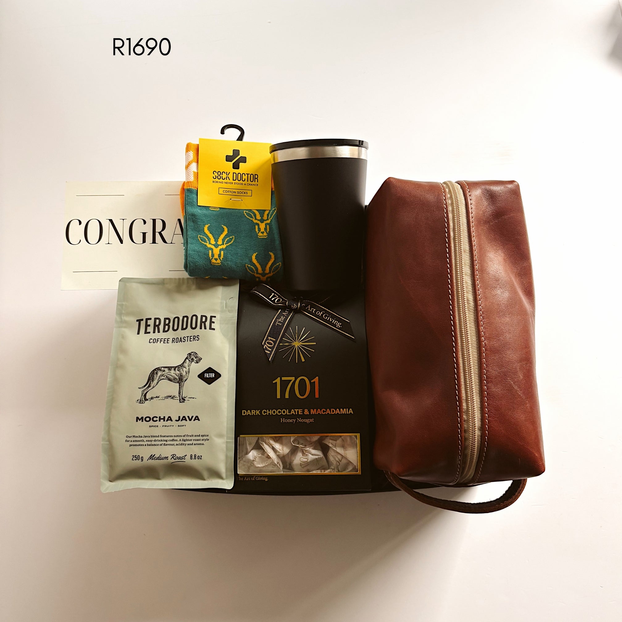 A curated gift set arranged on a white background, featuring a brown leather zip pouch, a black insulated tumbler, a bag of Terbodore coffee, a box of 1701 dark chocolate and magadama nougat, and a teal and yellow set of socks.